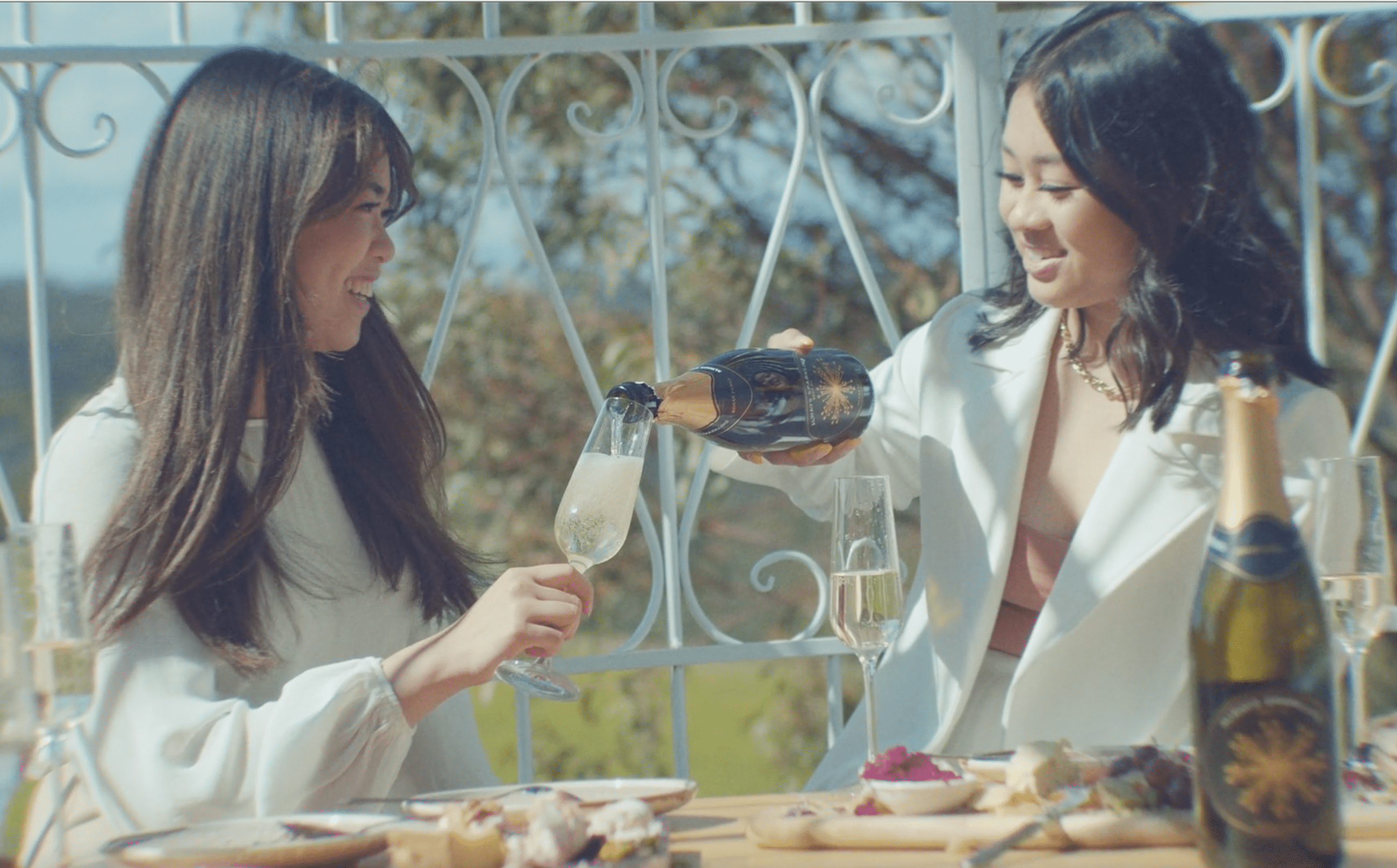 Two beautiful women in a winery sharing a bottle of sparkling wine