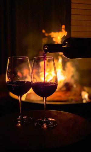 glowing bonfire with dancing flames shining light in red wine being poured from bottle into large wine glass
